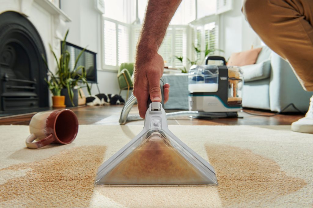 Close-up of a man using a VAX SpotWasher on a beige carpet